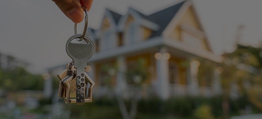 Hand holding keys in front of house.