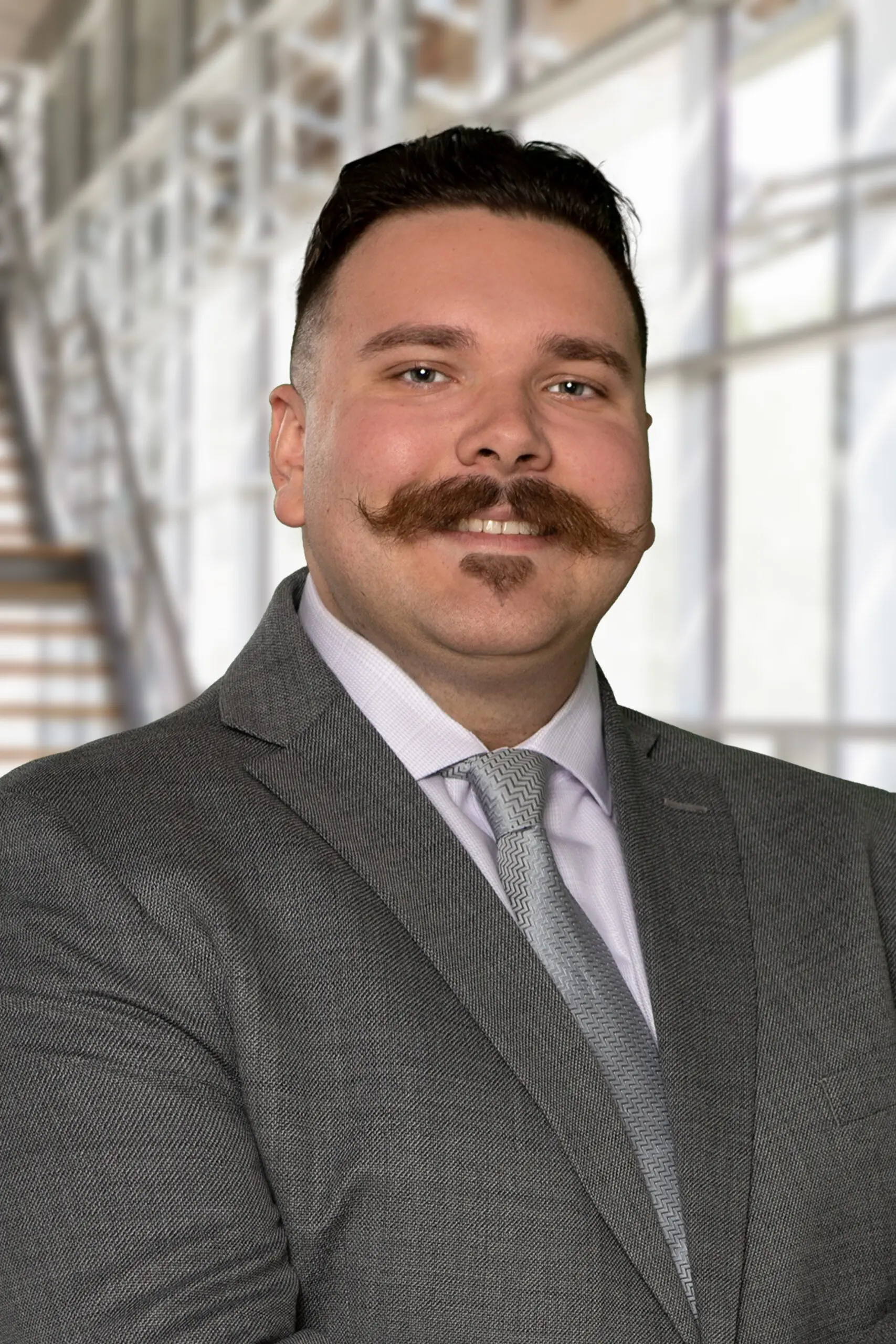 Man in a gray suit with a styled mustache and tie.